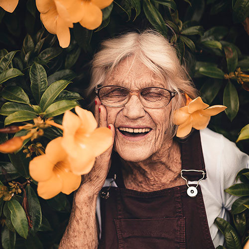 Elderly woman smiling amidst vibrant flowers. Joyful moment captured.